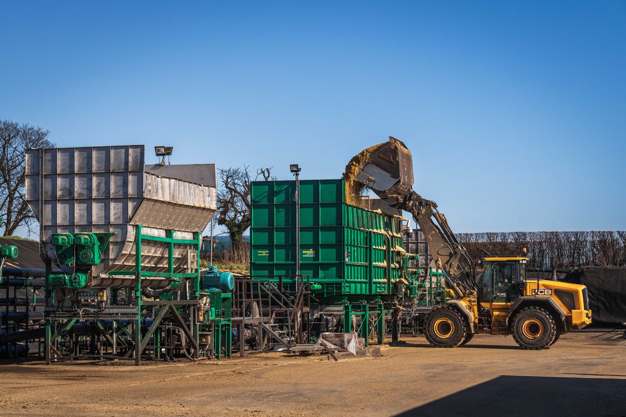 Yellow loader operating at a construction site with large green machinery under a clear blue sky.